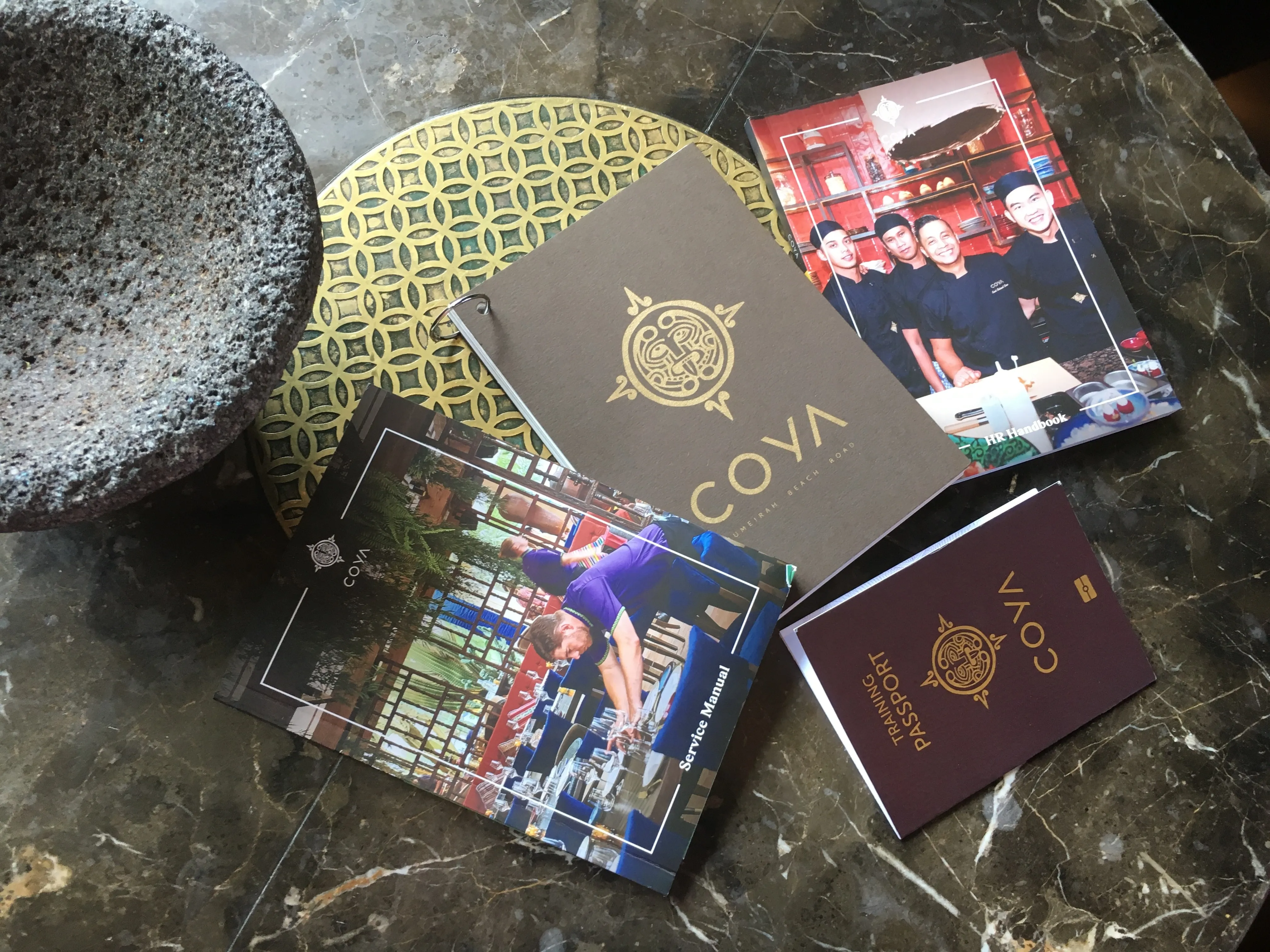 COYA printed training manuals and food and cocktail bibles stacked on a surface